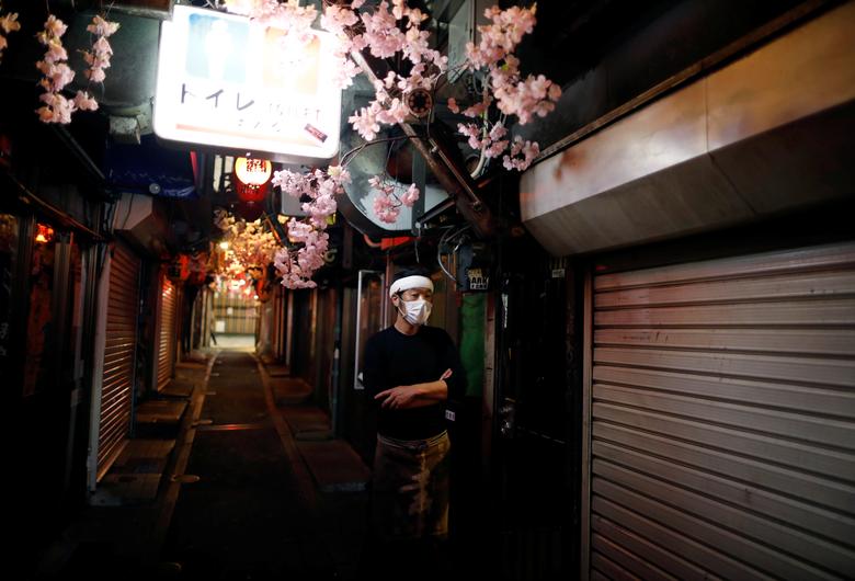 Япония. Работник ресторана в маске стоит на почти пустой аллее с барами после того как власти объявили коронавирусный карантин в Токио / апрель 2020 / Reuters